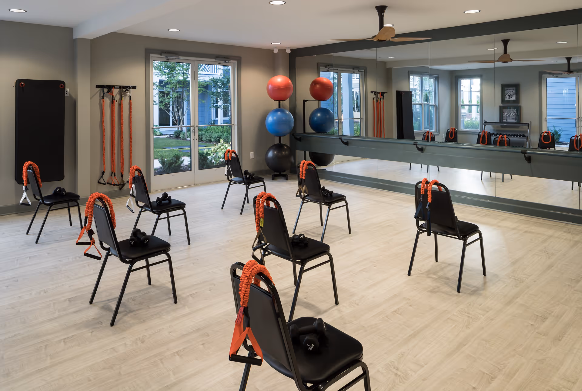 Bright fitness studio with spaced chairs, resistance bands, exercise balls, and a large mirrored wall.
