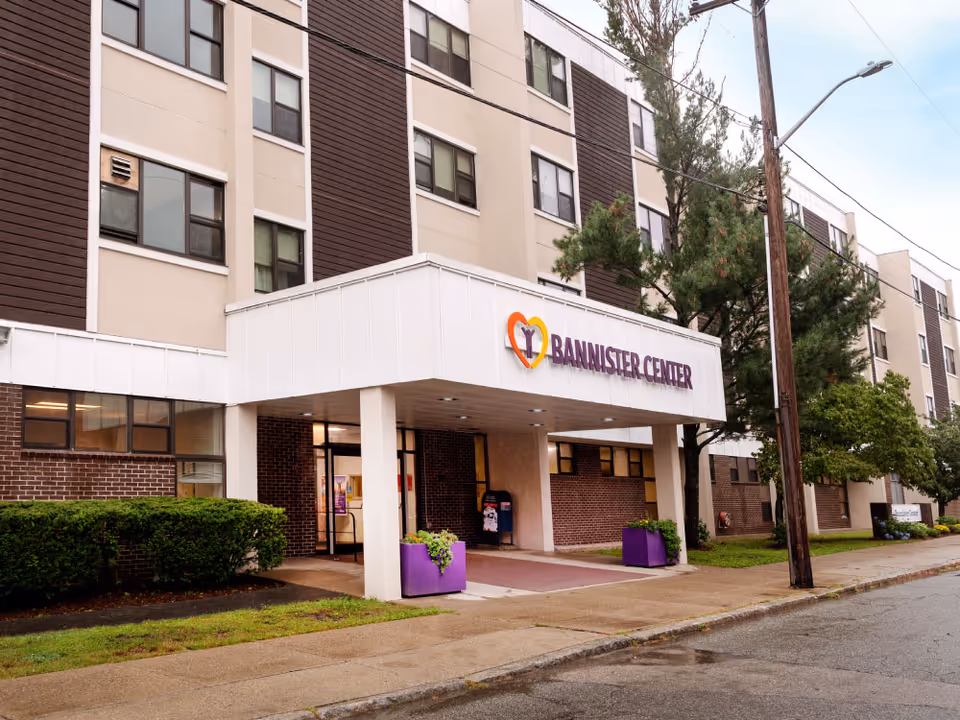 Exterior view of Bannister Center entrance with sign, planters, and surrounding trees.