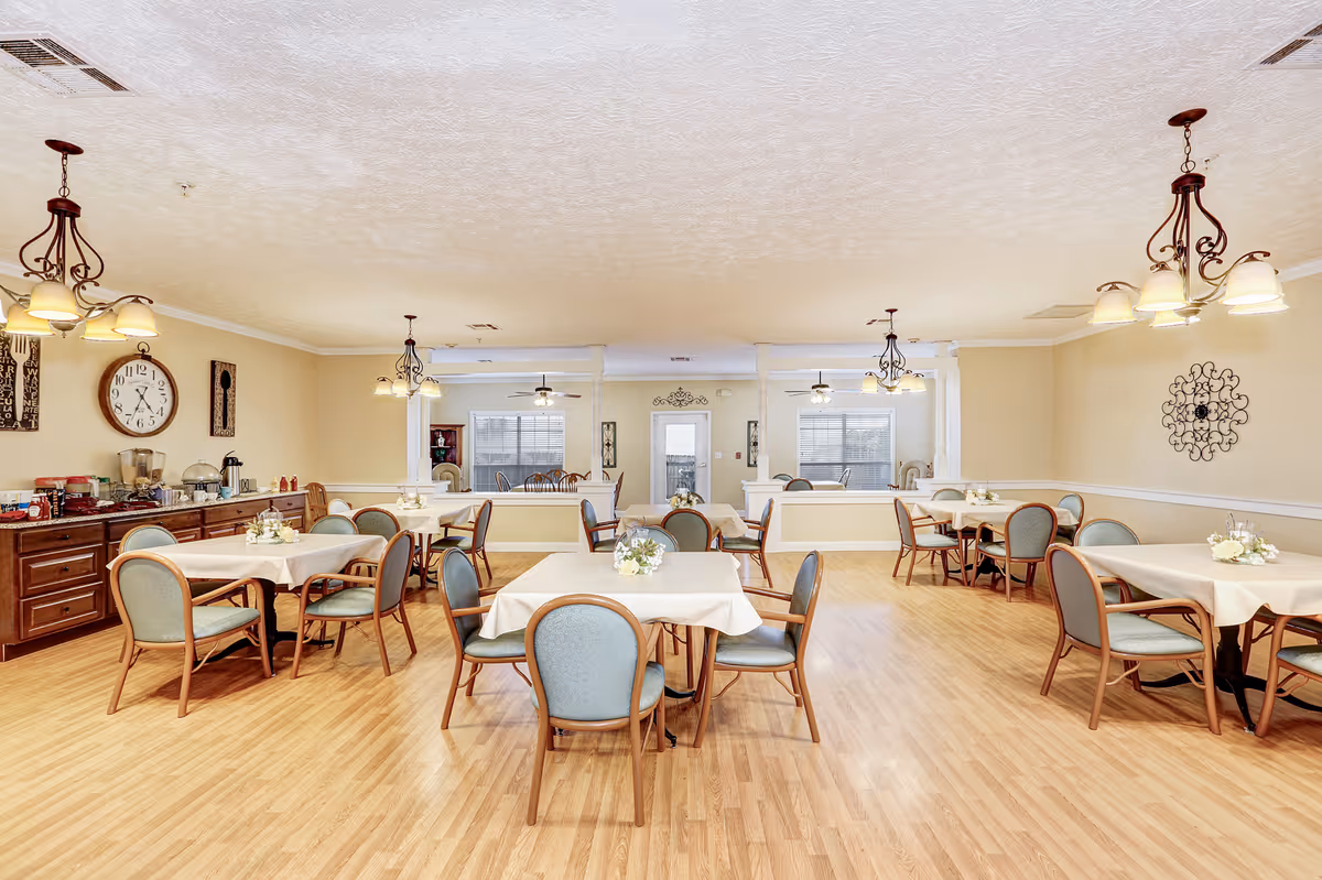 Spacious dining room with multiple tables and chairs, a buffet counter on the left, and hanging light fixtures.