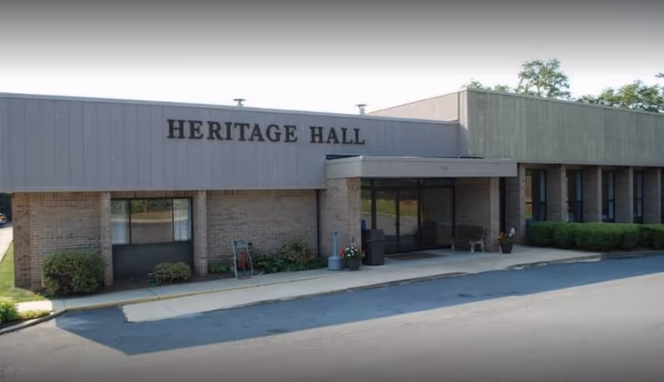 Front exterior of a single-story brick building with 'HERITAGE HALL' signage above a covered main entrance.