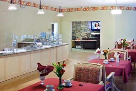 A dining room in a senior living facility with pink tablecloths and a buffet.