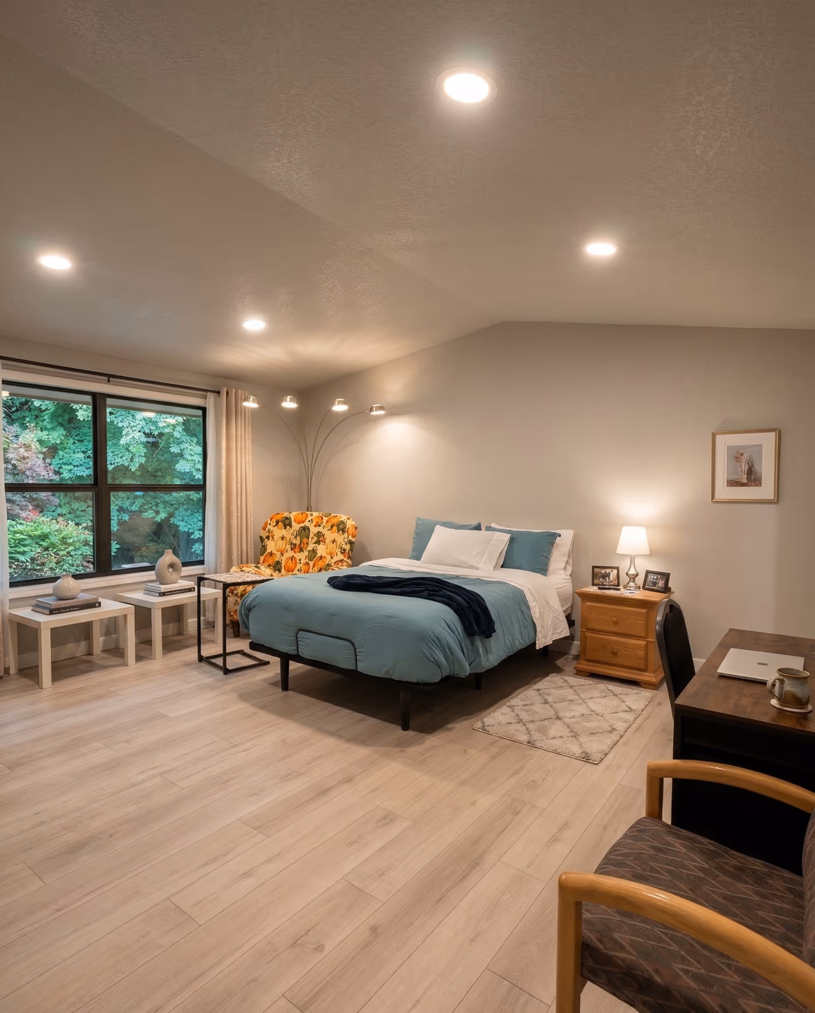 Bright, spacious senior living bedroom with a bed, seating area, and desk by a window.