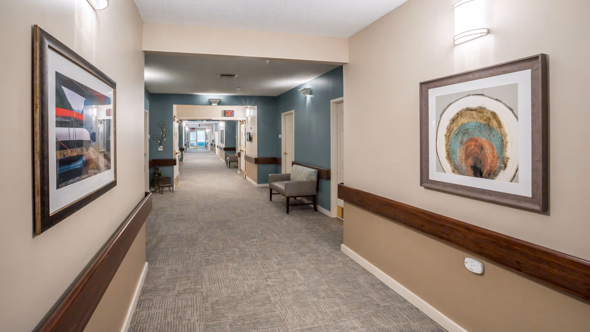 Carpeted interior hallway with framed artwork, handrails, seating, and doors along the corridor.