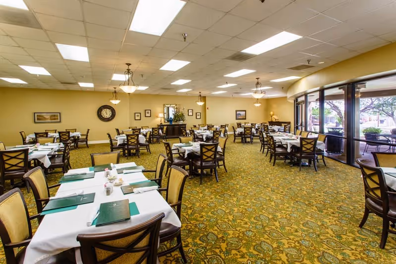 Spacious dining room with multiple set tables and chairs, chandeliers, and large glass doors opening to an outdoor patio.