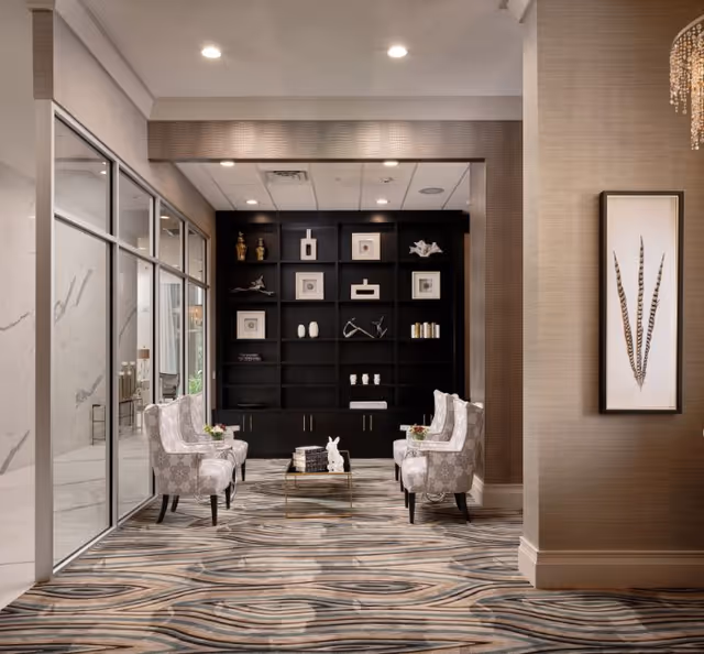 Sleek hotel-like lobby with two patterned armchairs, a glass door, and a dark bookcase.
