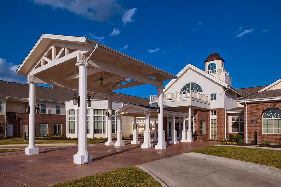 Covered entrance canopy and front facade of Crestview Retirement Community with white columns and brick exterior under a blue sky.