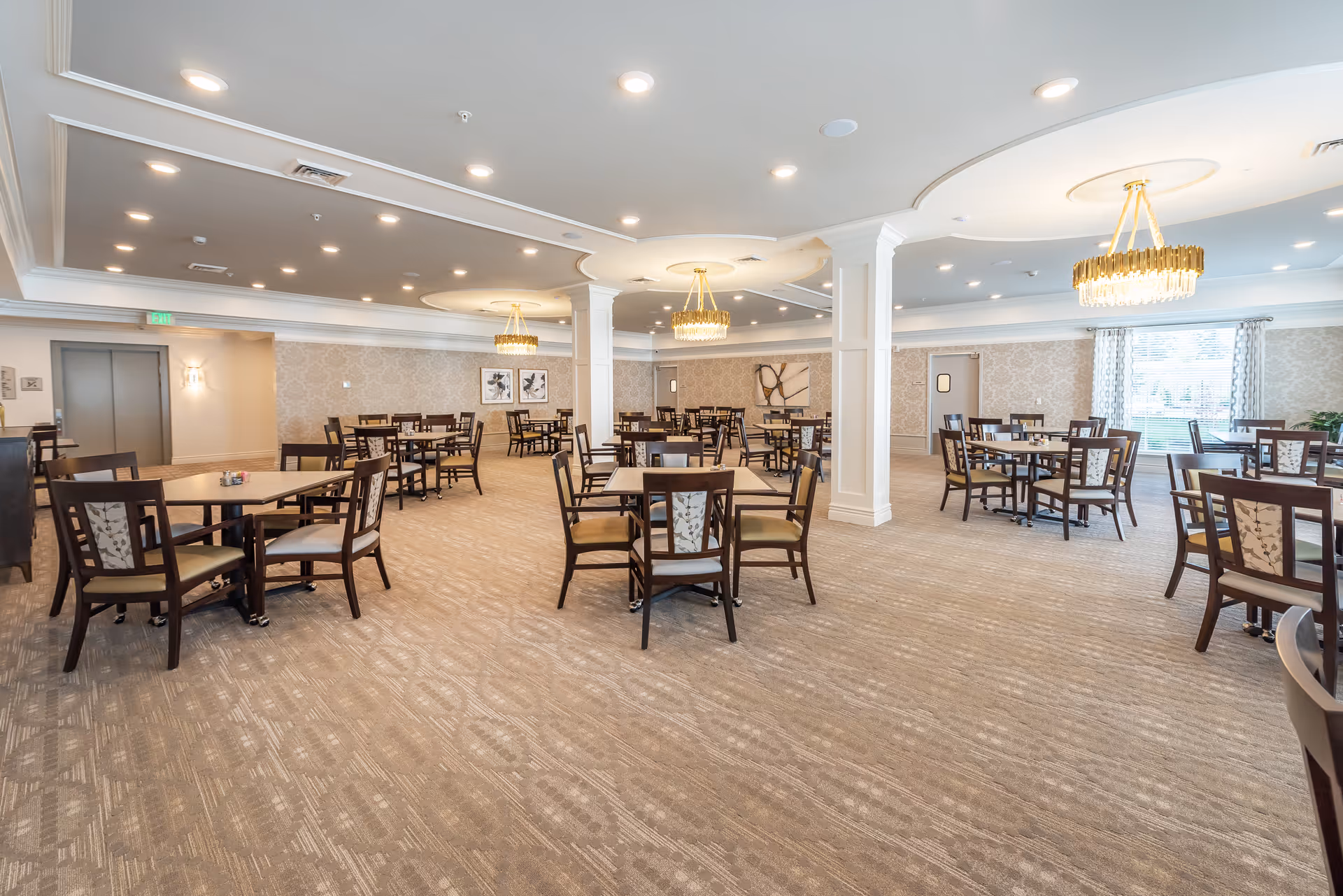 Spacious dining room with multiple tables and chairs, chandeliers, and patterned carpeting.
