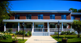 Front view of a brick senior living facility with white columns, stairs, and manicured lawn.
