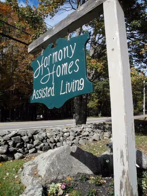 Green Harmony Homes Assisted Living sign on an outdoor post near trees.