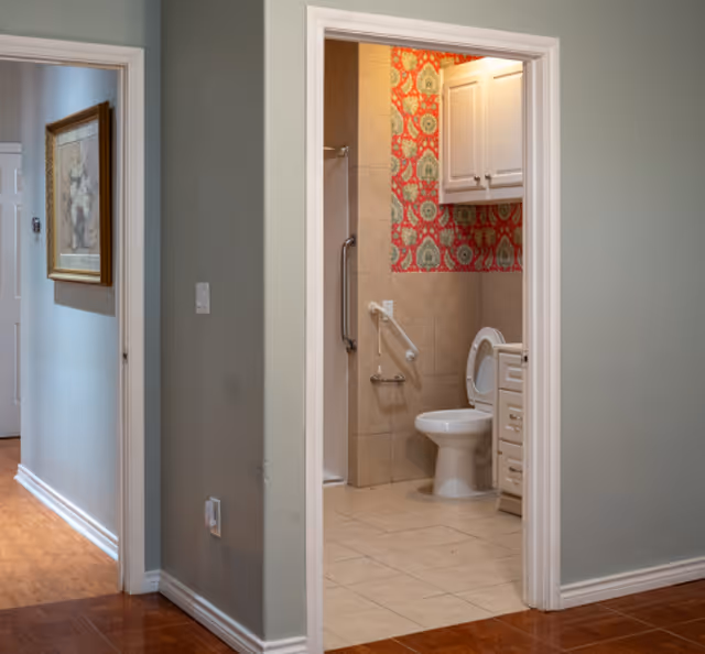 Doorway opens to a tiled bathroom with a toilet, cabinet, and patterned wallpaper.