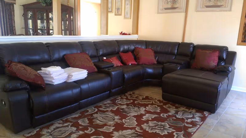 Large black leather sectional sofa in a living room with red pillows and a floral rug.