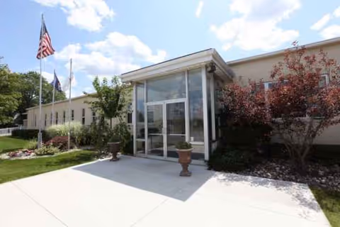 Front entrance of Laurels of Fulton with glass doors, flags, and landscaping.