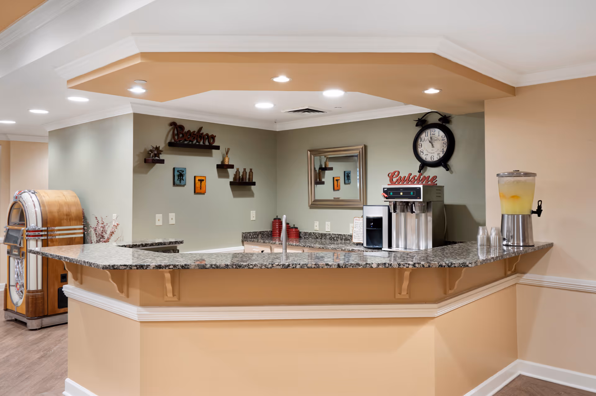 Granite-topped bistro counter with a coffee machine, juice dispenser and a jukebox in a senior living common area.