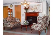 Small sitting room with floral-upholstered chairs and a loveseat around a coffee table in front of a fireplace and chandelier.