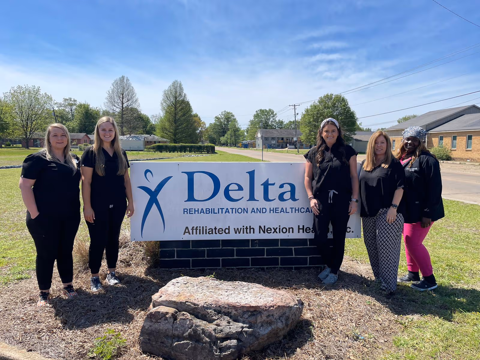 Six staff standing outside next to a Delta Rehabilitation and Healthcare sign on the facility's lawn.