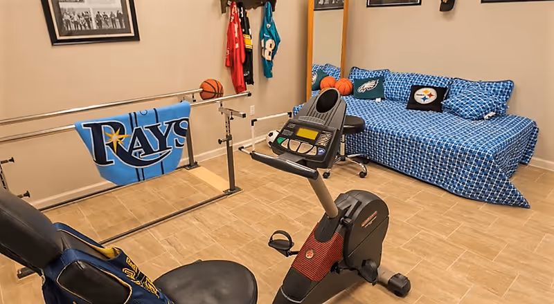 Interior therapy room with an exercise bike, parallel bars, and a sports-themed daybed.