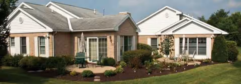 Single-story brick senior living facility front exterior with landscaping and outdoor seating.