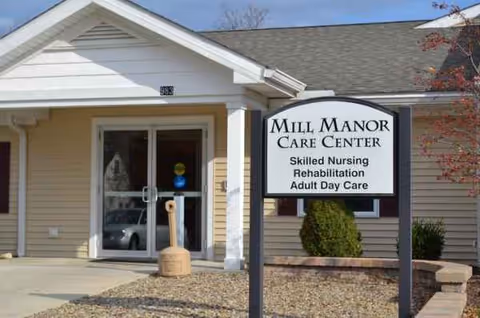 Exterior view of Mill Manor Care Center entrance with a prominent sign and driveway.