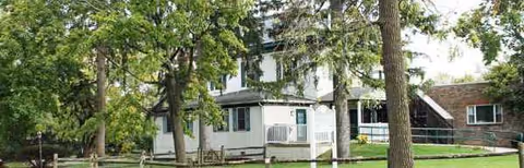 Exterior view of a white senior care facility with a small porch and trees.