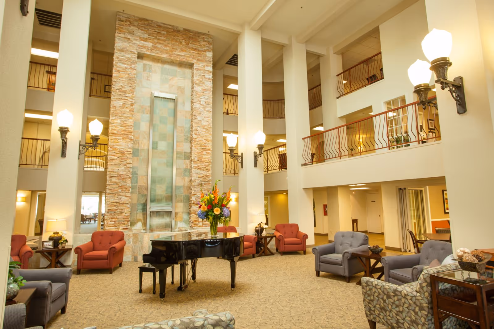 Spacious multi-level atrium lounge with a grand piano, seating areas, and a tall decorative water feature.