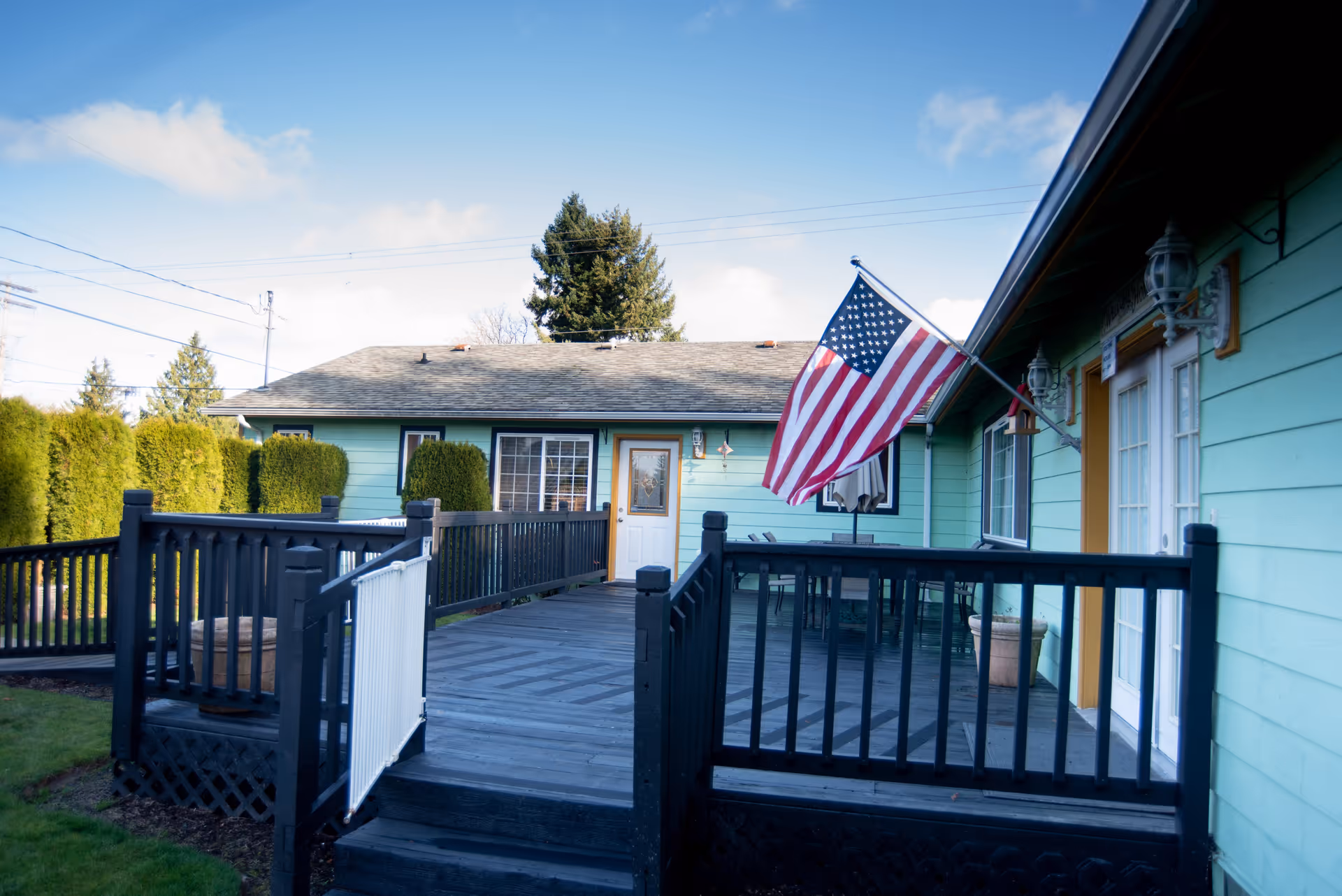 Wooden ramp and porch leading to the front doors of a mint-green building with an American flag.