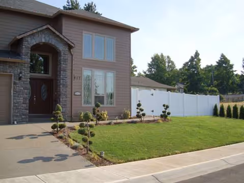 Two-story brown senior living home with stone arch entry, manicured lawn, and white fence.