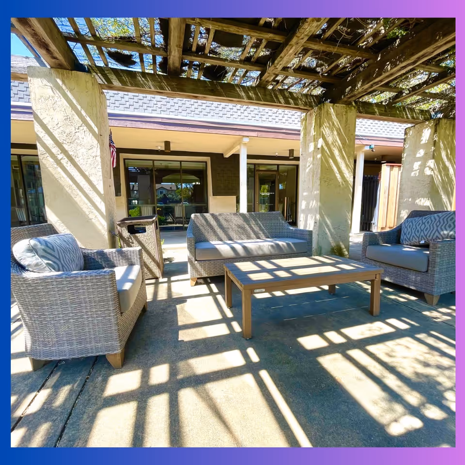 Outdoor covered patio with wicker sofas and a coffee table under a wooden pergola casting patterned shadows.