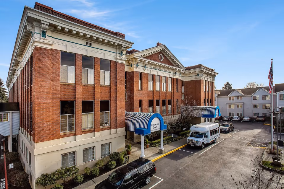 Exterior view of Washington Oakes facility with brick facade, blue canopies, and parked vehicles.