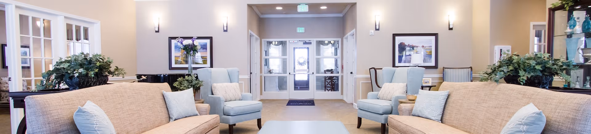Spacious senior living lobby with sofas and armchairs arranged around a central coffee table facing the entrance.