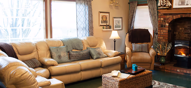 Cozy living room with a beige leather sofa, matching armchair, brick fireplace, and a wicker coffee table.