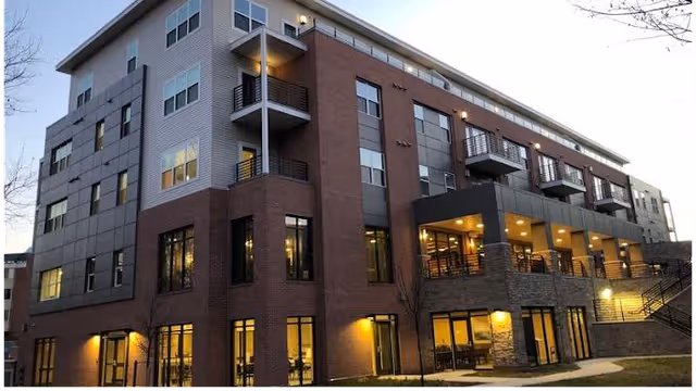 Modern multi-story senior living building exterior at dusk with lit windows and balconies.
