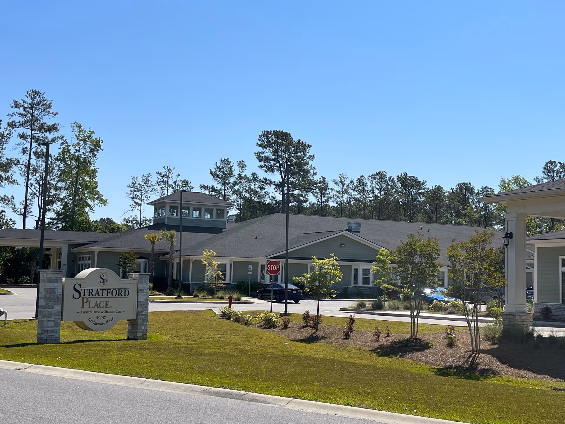 Exterior front of Stratford Place assisted living building with entrance sign and landscaped lawn under a clear blue sky.