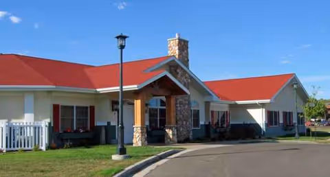 A single-story senior living facility with a red roof and stone chimney in front.