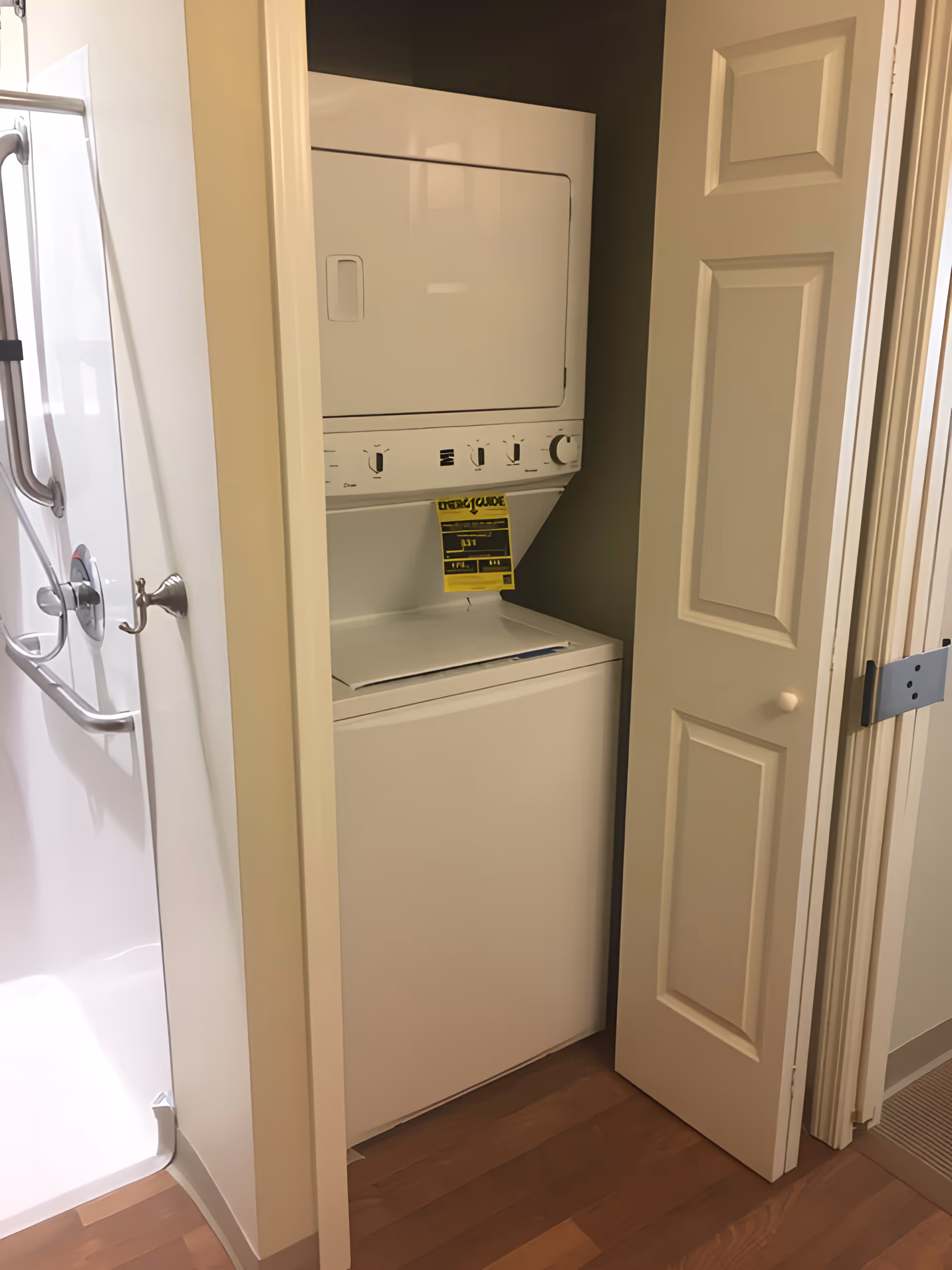 Stacked washer and dryer in a small closet with the bifold door open next to a shower stall.