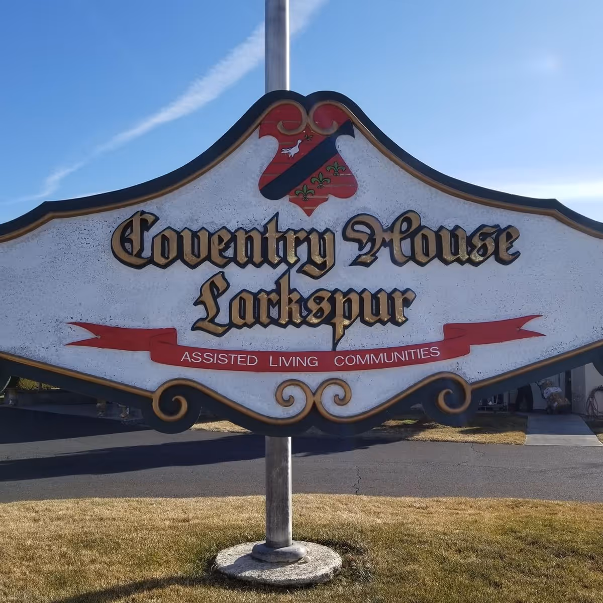 A decorative outdoor sign for Coventry House Larkspur Assisted Living Communities mounted on a metal pole with a clear blue sky in the background.