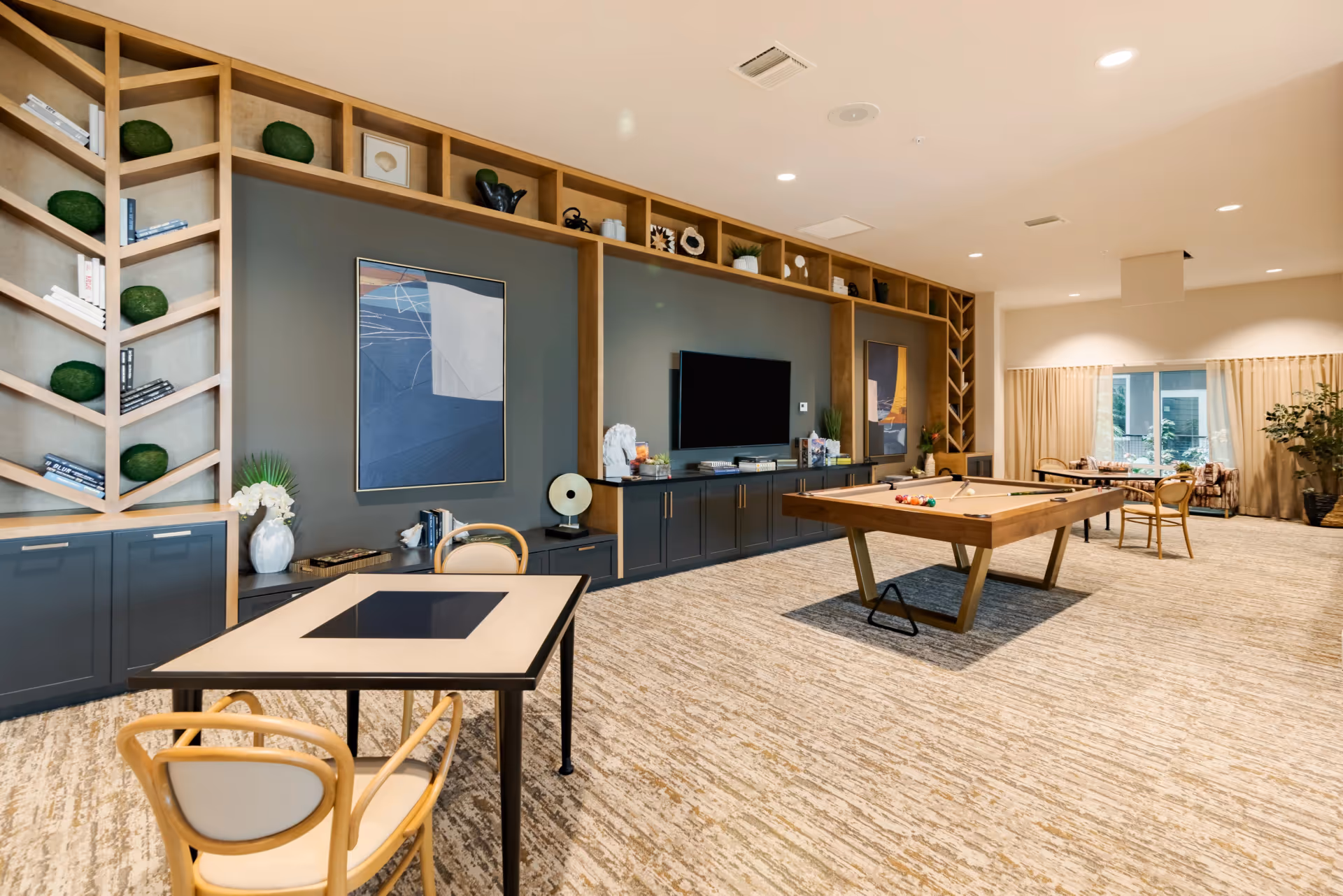 Spacious senior living common room with a pool table, TV, shelving, and multiple seating areas.