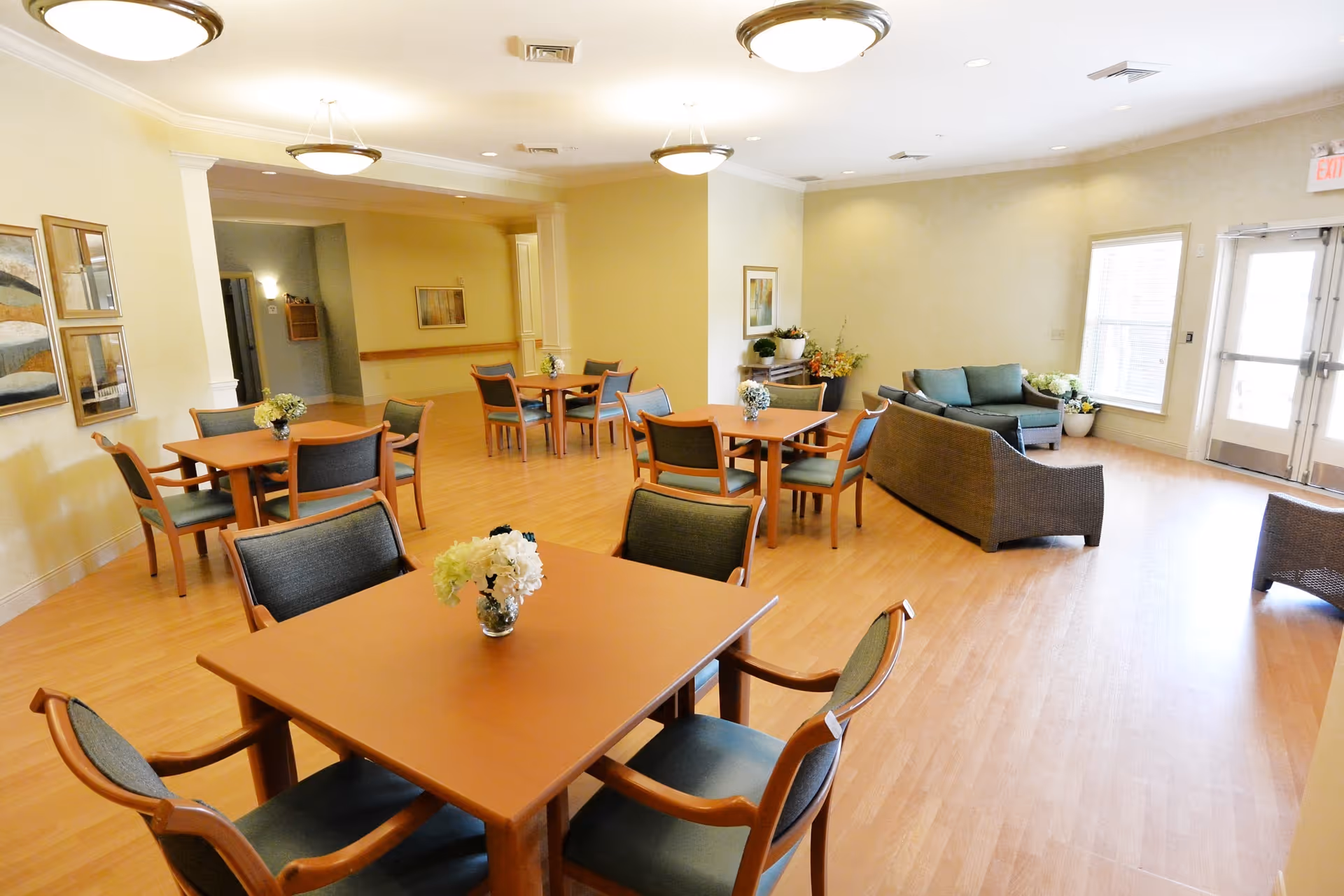 Bright communal dining and lounge room with several wooden tables and chairs and a seating area with sofas.