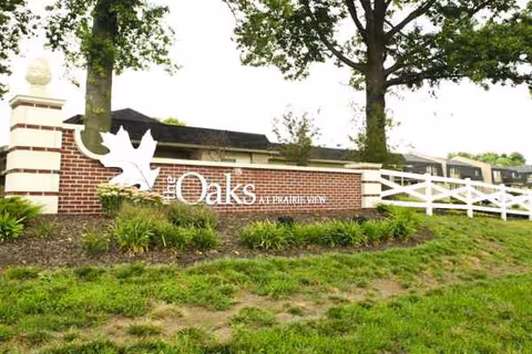 Exterior view of The Oaks facility sign on brick wall with greenery.