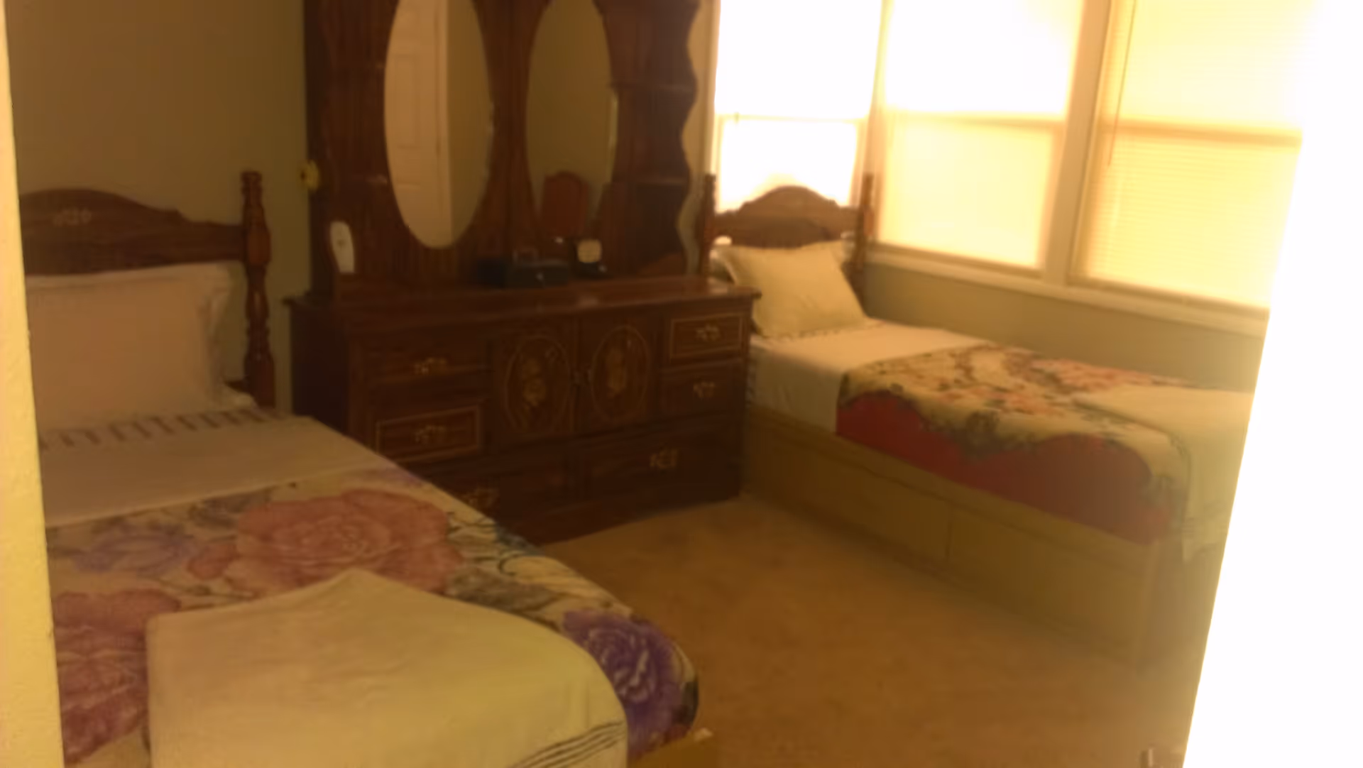 Two single beds in a softly lit bedroom with a wooden dresser and mirror between windows.