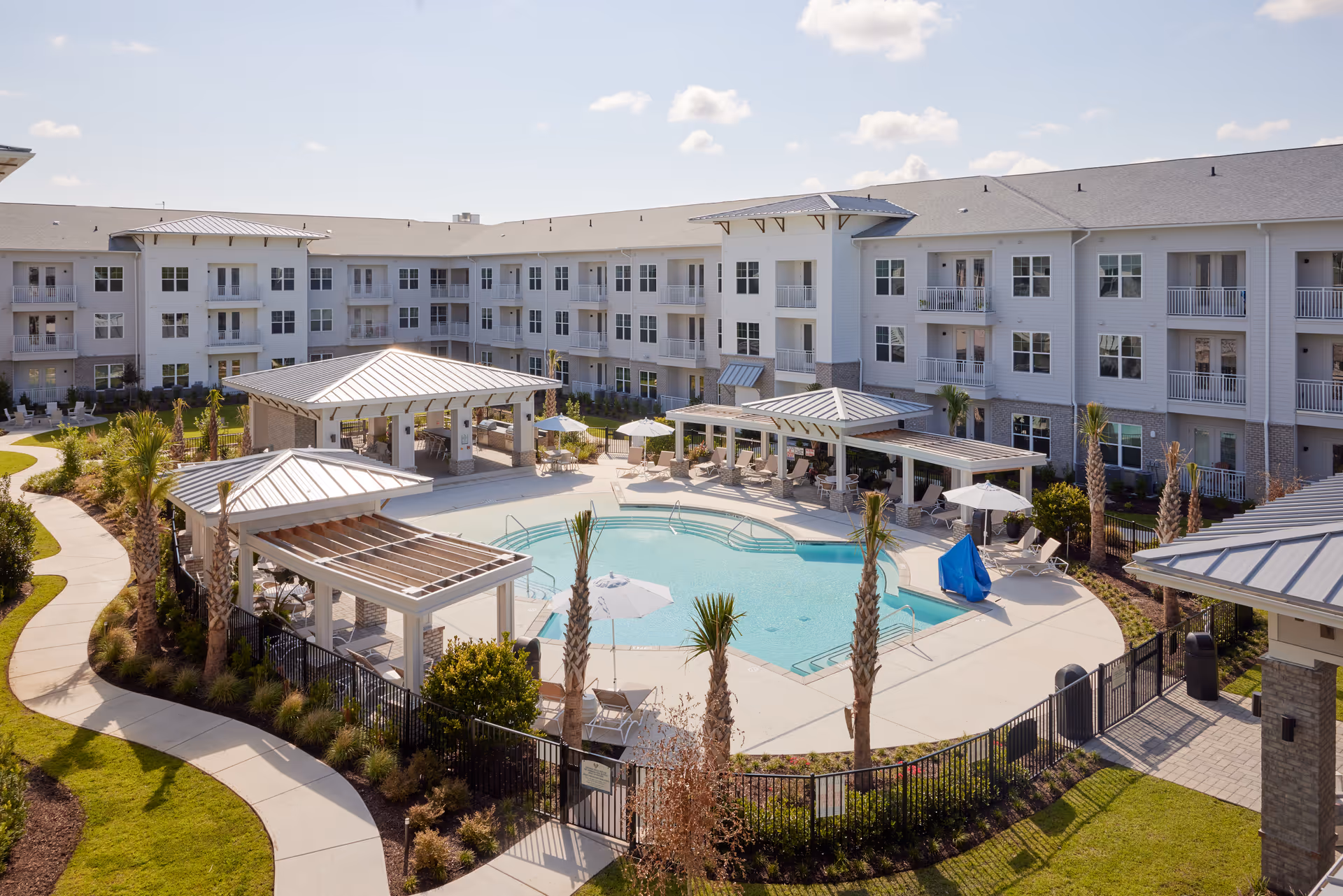 Outdoor central swimming pool with cabanas, lounge chairs and landscaped walkways surrounded by a three-story residential building.