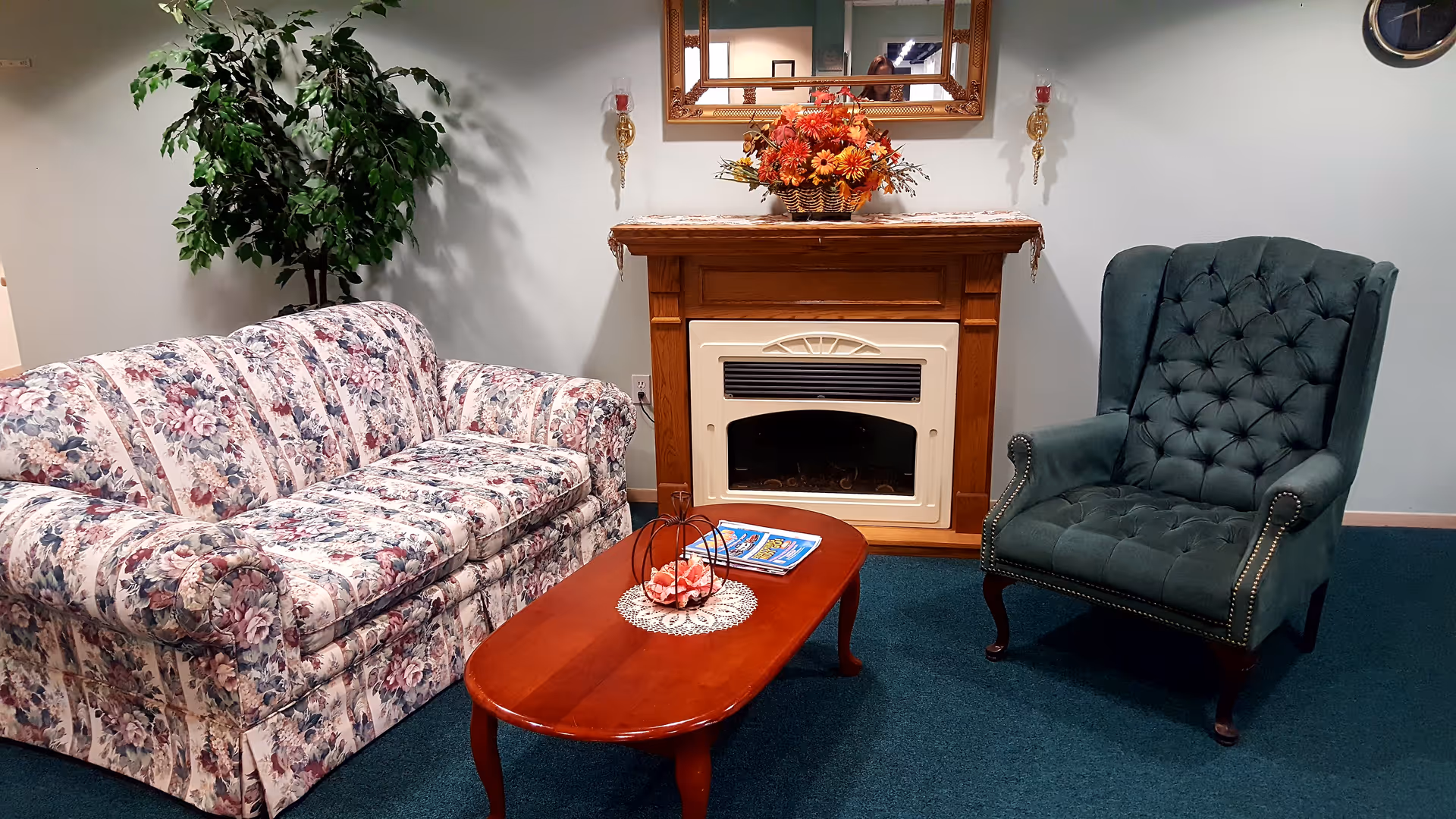 Cozy sitting area with a floral sofa, green tufted armchair, wooden coffee table and a decorative fireplace mantel.