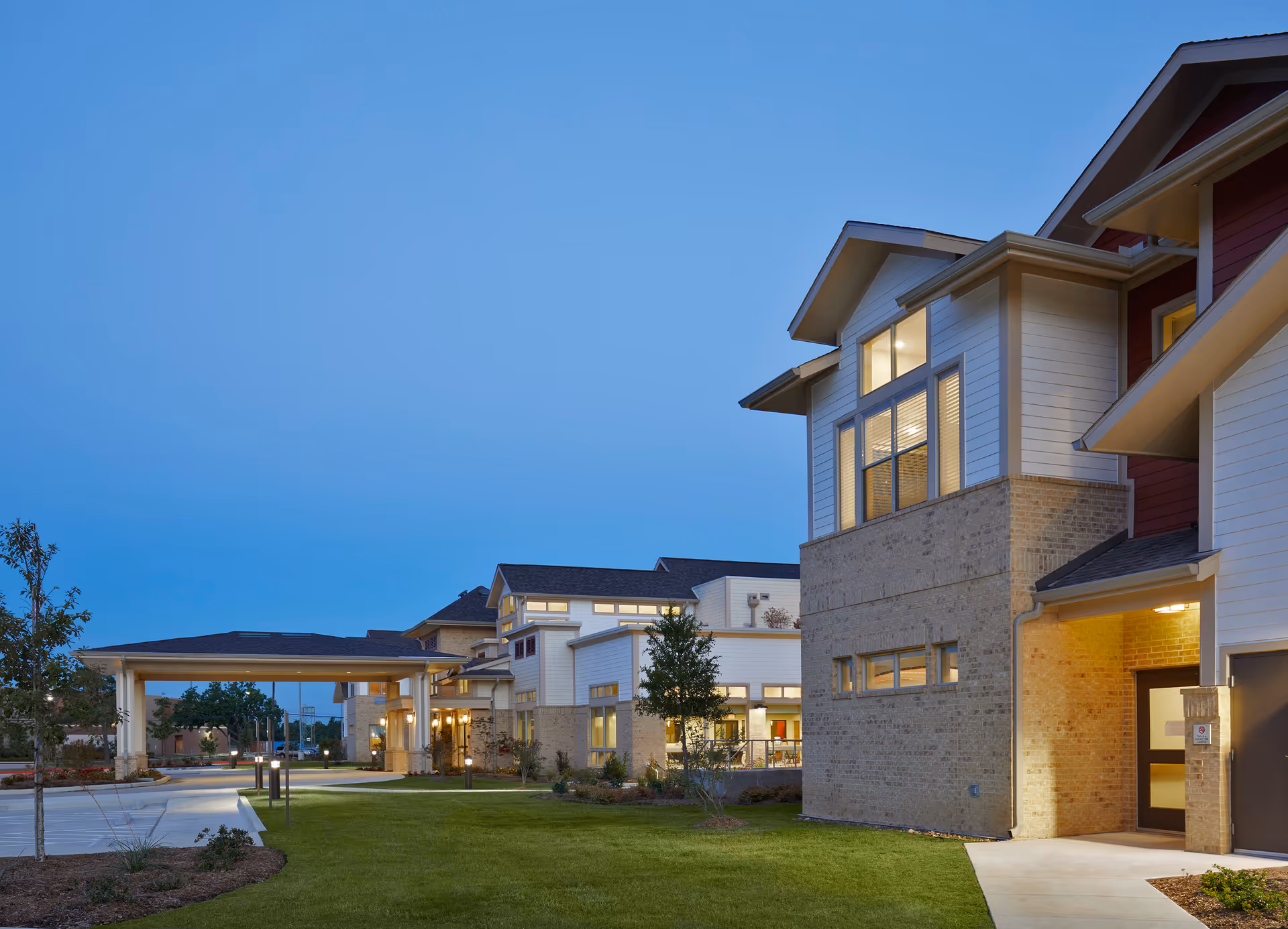 Exterior view of a modern senior living facility building at dusk with well-maintained landscaping and a covered entrance.