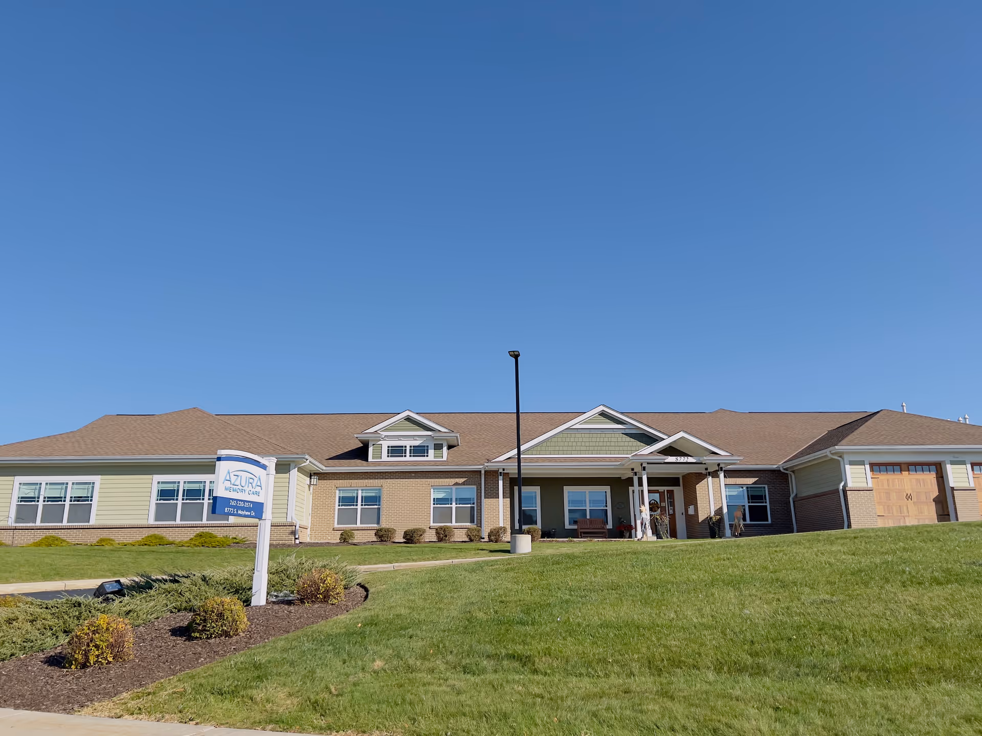 Exterior view of Azura Memory Care of Oak Creek building with a clear blue sky, green lawn, and a sign in front displaying the facility name and contact information.