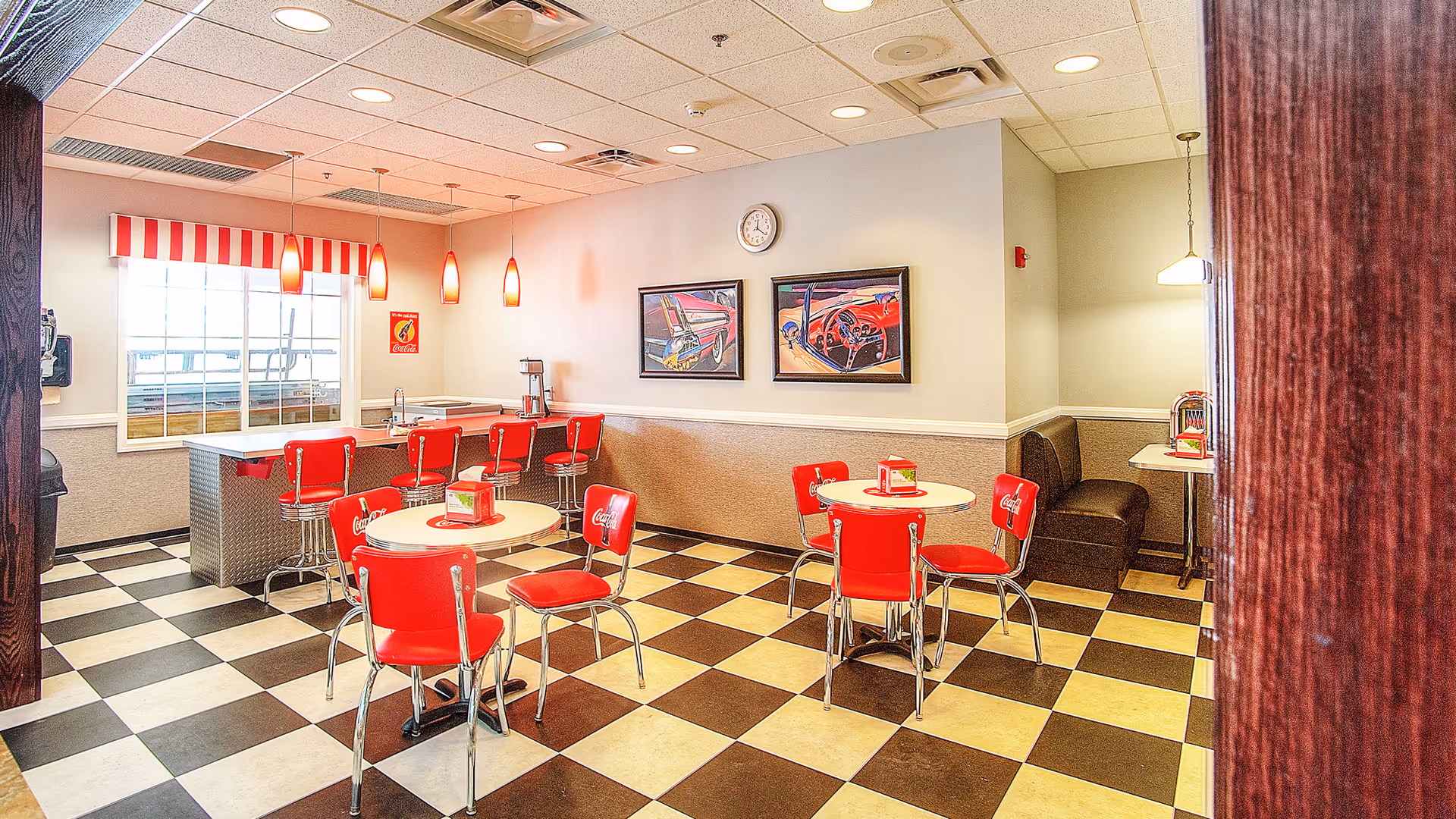 Retro diner-style dining area with red chairs and booths, a black-and-white checkered floor, and a counter with stools.