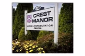A freestanding sign reading "Crest Manor Living & Rehabilitation Center" surrounded by shrubs and yellow flowers.