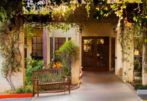 Exterior entrance to a senior living facility with a bench and climbing vines.