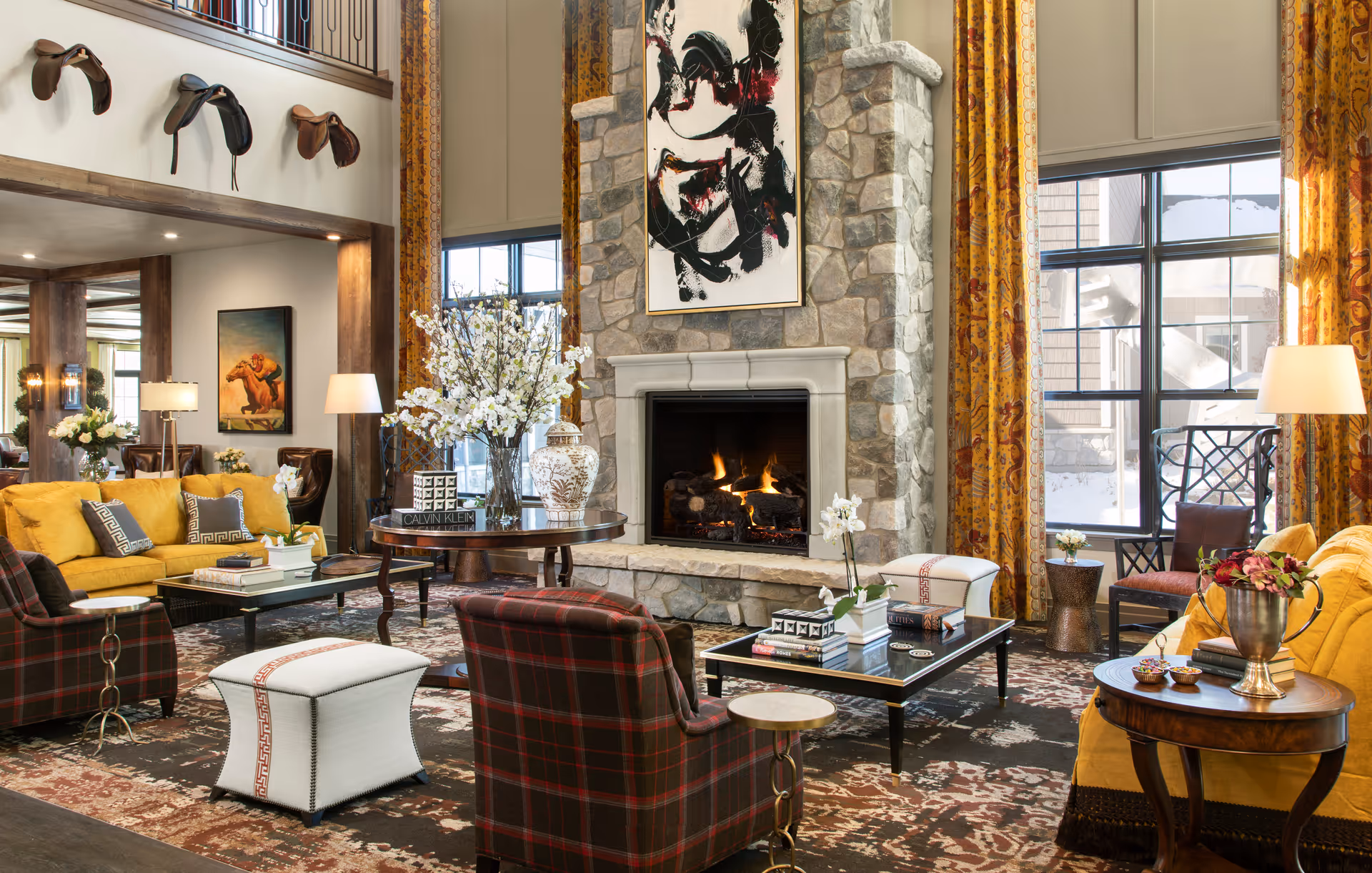 Elegant communal living room with sofas and armchairs arranged around a stone fireplace and large windows.