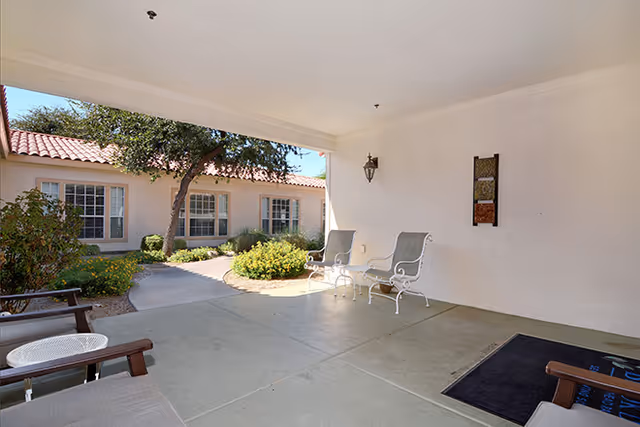 Covered outdoor seating area and walkway in front of a single-story building with a tiled roof and landscaping.