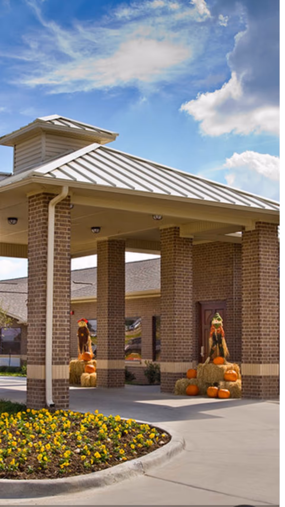 Exterior view of a brick building entrance with fall pumpkin decorations under a covered walkway.