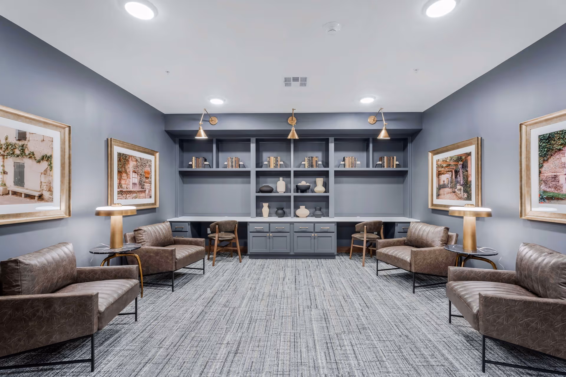 Modern lounge with leather chairs, side tables, built-in shelving and framed artwork under soft lighting.